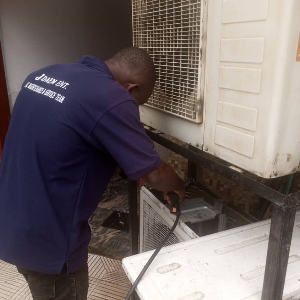 JDAEM technician carrying out routine maintenance on an outdoor AC condenser